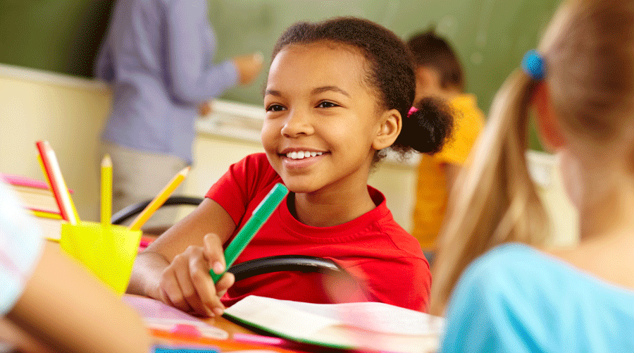 微笑的女孩的图象在教室的，拿着蜡笔