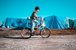 图像的叙利亚男孩骑自行车在一个难民营