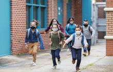 孩子们在学校外跑步的图像，戴着口罩